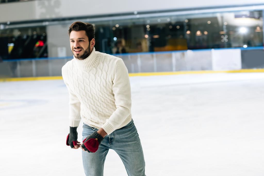 knappe man in jeans en trui schaatsen op ijsbaan - Foto, afbeelding