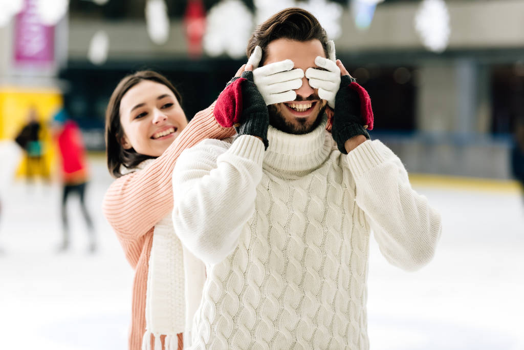 happy girl closing eyes to smiling man to make a surprise on skating rink   - Photo, Image
