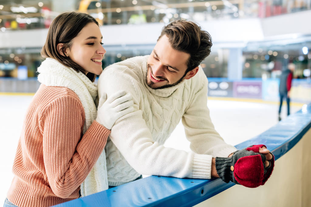 cheerful young couple in sweaters spending time on skating rink   - 写真・画像
