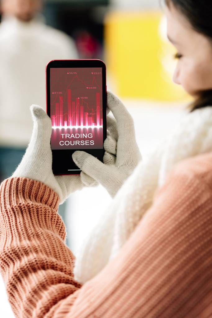 обрізаний вид жінки в рукавичках, що тримає смартфон із додатком торгових курсів на екрані
 - Фото, зображення