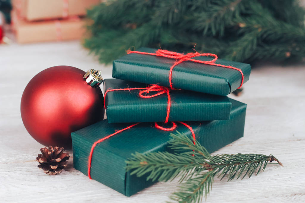 Крупный план зеленых рождественских подарочных коробок, красных безделушек, елок ветвей, конуса. Концепция рождественских подарков Новый год, зимний праздник, подарок, экопакет, праздник
 - Фото, изображение