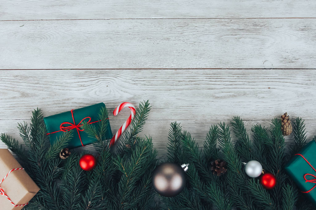 Concetto di sfondo natalizio. Palline di Natale rosse, rami di abete, confezione regalo verde, canna da zucchero, coni su tavolo di legno bianco. Capodanno, vacanza invernale, copia lo spazio, vista dall'alto
 - Foto, immagini