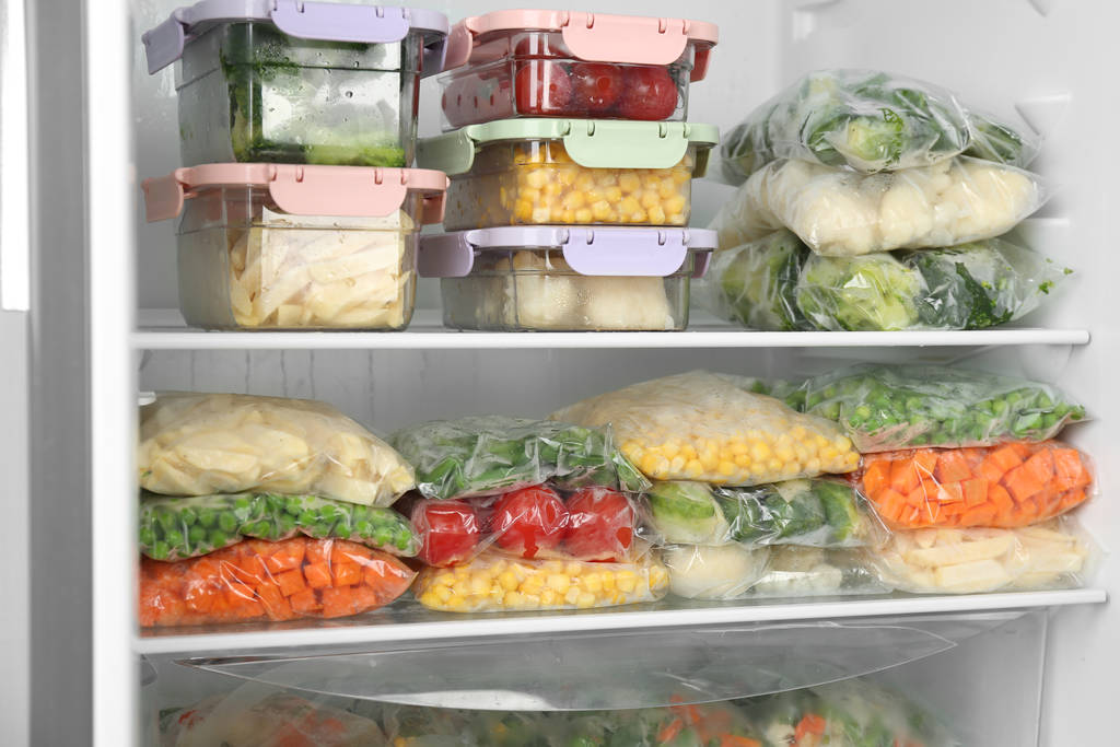 Plastiktüten und Behälter mit verschiedenem Tiefkühlgemüse im Kühlschrank - Foto, Bild