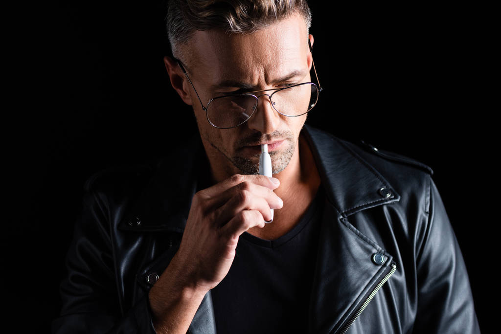 KYIV, UKRAINE - LOKAKUU 11, 2019: Komea mietteliäs mies tupakointi iqos eristetty mustalla
  - Valokuva, kuva