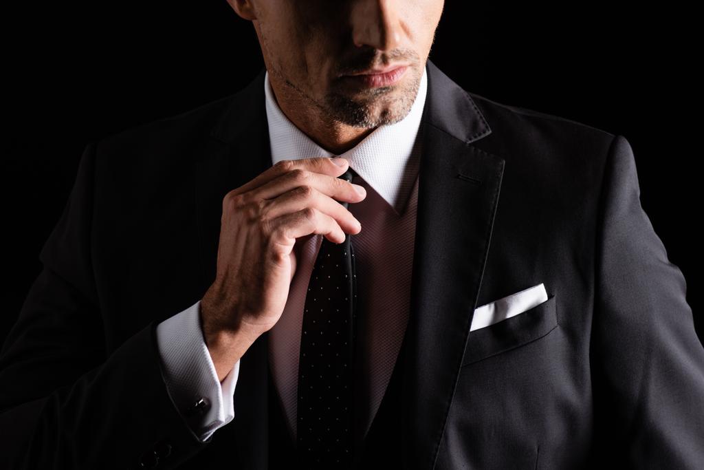 Oříznutý pohled na podnikatele, upravující kravatu izolovanou na černém - Fotografie, Obrázek