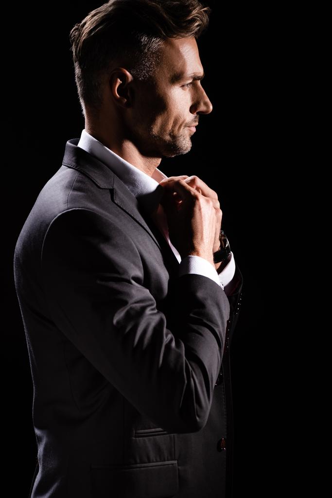 Side view of businessman buttoning up shirt isolated on black - Photo, Image
