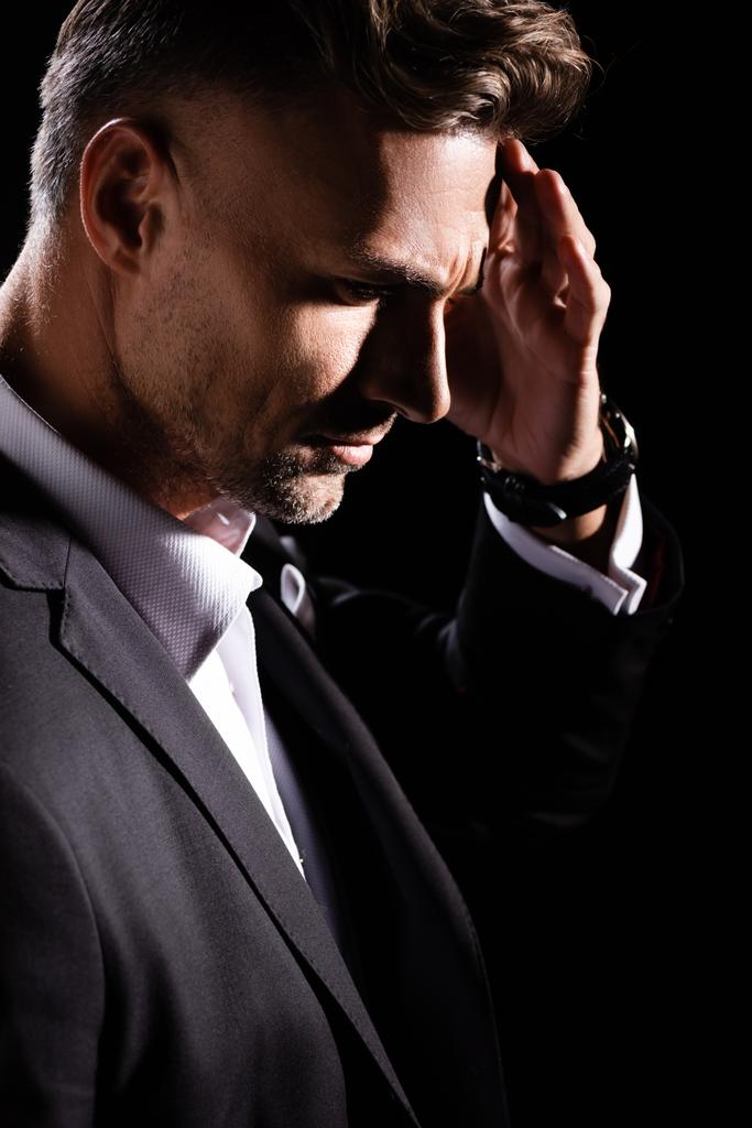 Seitenansicht des nachdenklichen Geschäftsmannes mit der Hand am Kopf, der isoliert auf schwarz herabblickt  - Foto, Bild