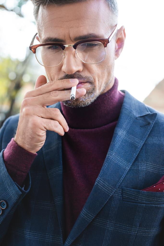 Красивый бизнесмен курит сигарету и смотрит на улицу
 - Фото, изображение