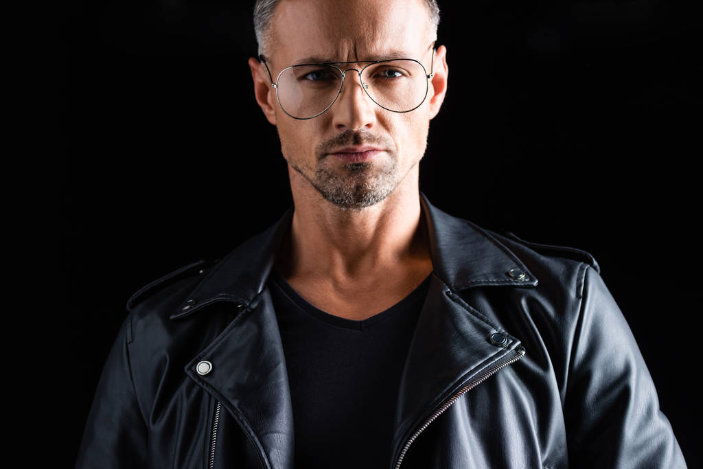 Confident stylish man in sunglasses and leather jacket looking at camera isolated on black - Photo, Image