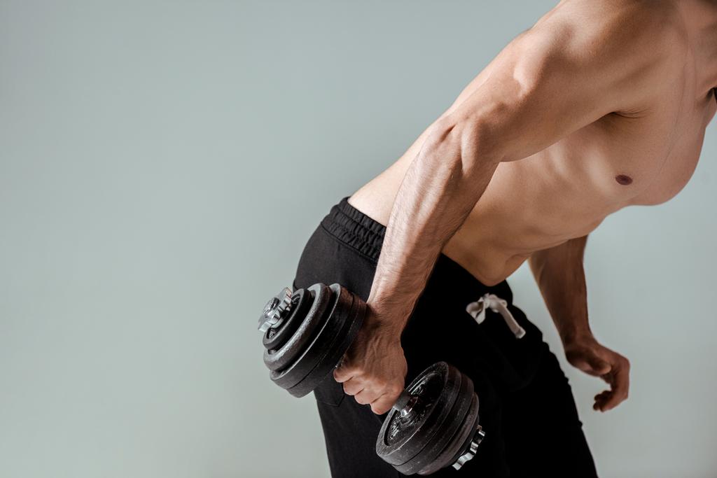 Teilansicht sexy muskulöser Bodybuilder mit nacktem Oberkörper beim Training mit Kurzhantel isoliert auf grau - Foto, Bild