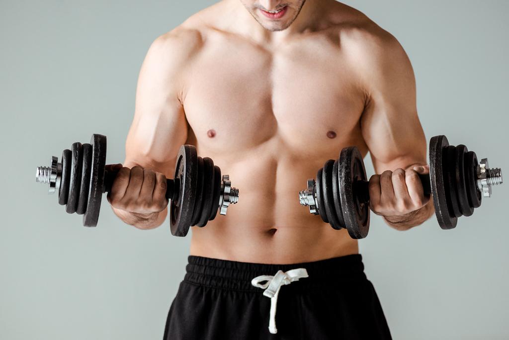 μερική άποψη της σέξι μυϊκή bodybuilder με γυμνό κορμό άσκηση με αλτήρες απομονώνονται σε γκρι - Φωτογραφία, εικόνα