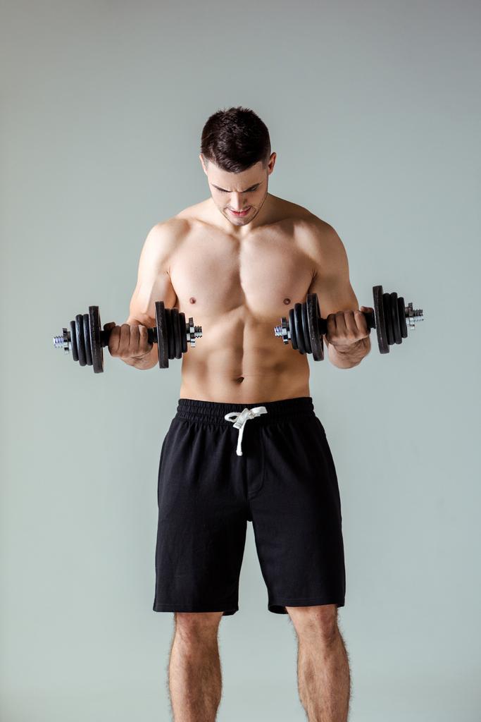 seksikäs lihaksikas kehonrakentaja, jolla on paljas vartalo, joka käyttää harmaalla eristettyjä käsipainoja
 - Valokuva, kuva