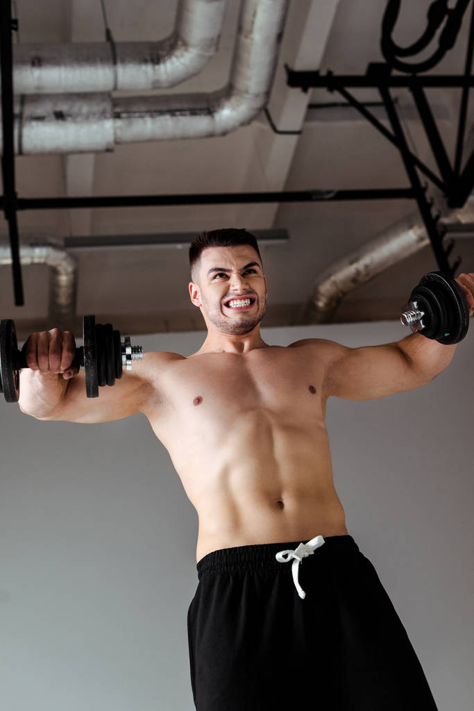 άποψη χαμηλή γωνία σέξι μυϊκή bodybuilder με γυμνό κορμό άσκηση με αλτήρες - Φωτογραφία, εικόνα