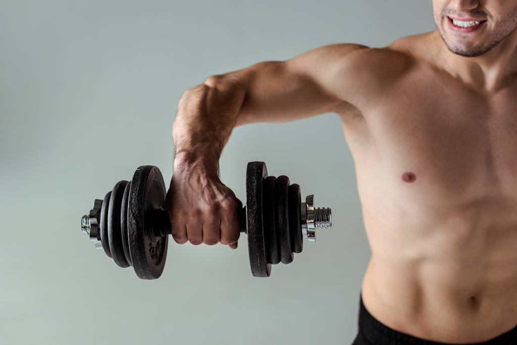 partial view of sexy muscular bodybuilder with bare torso exercising with dumbbell isolated on grey - Photo, Image