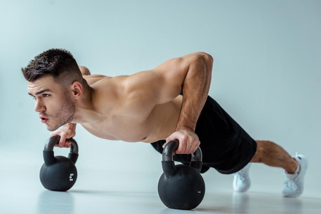 fisiculturista muscular sexy com tronco nu fazendo flexões com kettlebells em cinza
 - Foto, Imagem