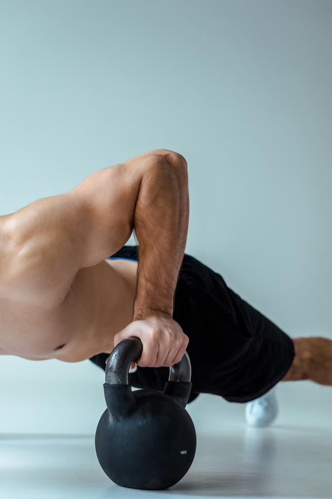 osittainen näkymä seksikäs lihaksikas kehonrakentaja paljain vartalo tekee push ups kettlebell harmaa
 - Valokuva, kuva