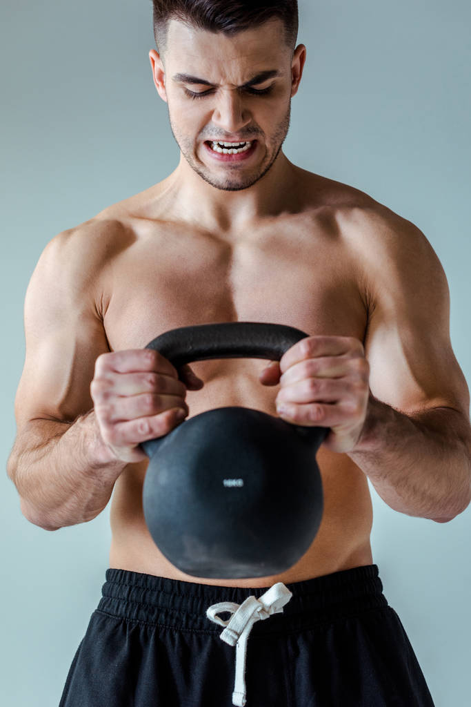 tense sexy muscular bodybuilder with bare torso exercising with kettlebell isolated on grey - Photo, Image