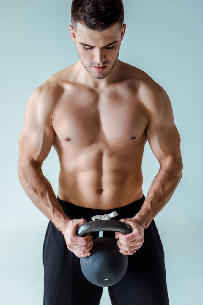 sexy musculoso culturista con torso desnudo ejercitando con kettlebell aislado en gris
 - Foto, imagen