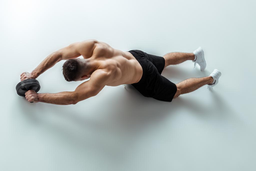 visão aérea do fisiculturista muscular sexy com tronco nu exercitando com roda ab no fundo cinza
 - Foto, Imagem