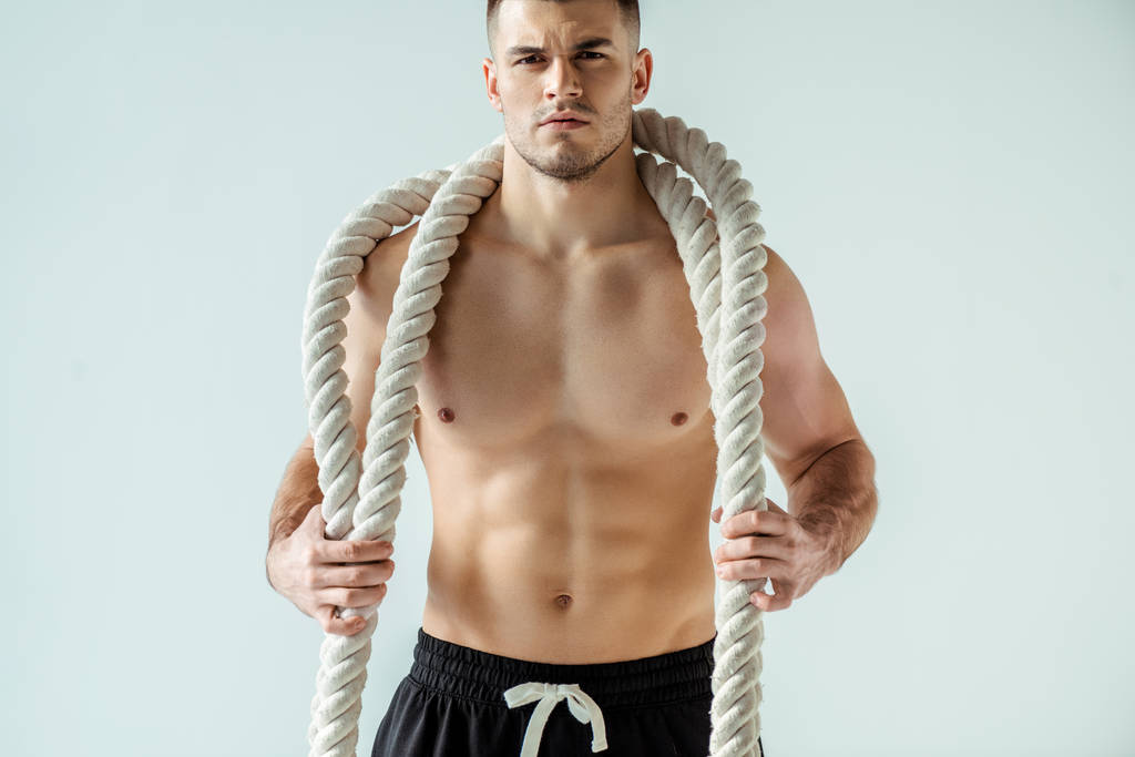 sexy muskulöser Bodybuilder mit nacktem Oberkörper posiert mit Kampfseil isoliert auf grau - Foto, Bild