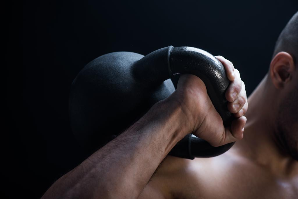 Ausgeschnittene Ansicht muskulöser Bodybuilder beim Exzidieren mit Kettlebell isoliert auf Schwarz - Foto, Bild