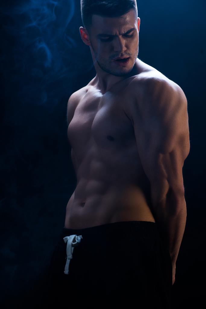 σέξι μυώδης bodybuilder με γυμνό κορμό σε μαύρο φόντο με καπνό - Φωτογραφία, εικόνα