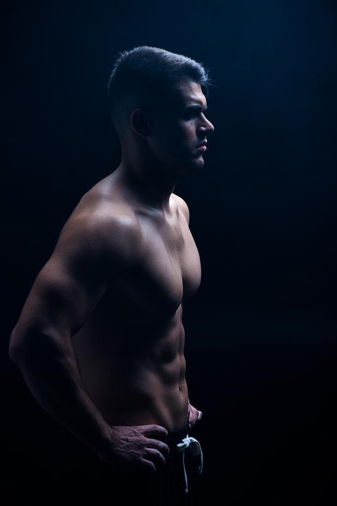 Seitenansicht von sexy muskulösen Bodybuilder mit nacktem Oberkörper posiert mit Händen auf Hüften isoliert auf schwarz - Foto, Bild