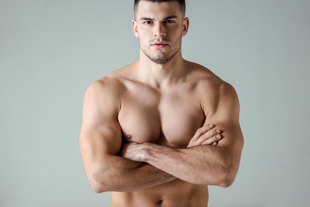 sexy gespierde bodybuilder met kale romp poseren met gekruiste armen geïsoleerd op grijs - Foto, afbeelding