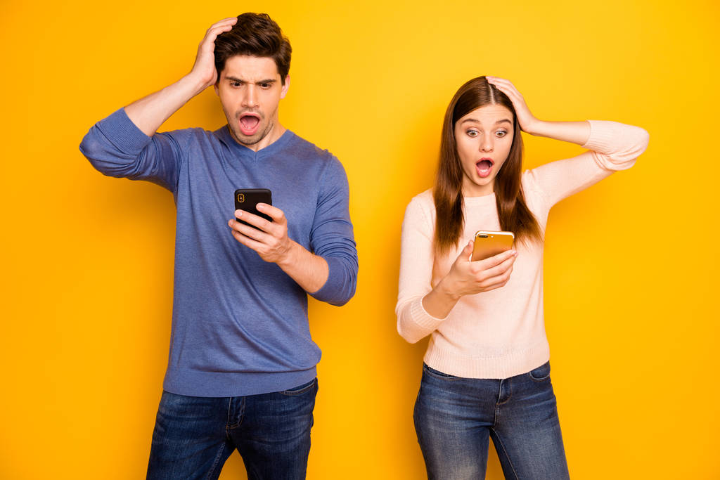 Impresionante blogger pareja romántica uso smartphone leer noticias grito wow omg desgaste azul suéter rosa vaqueros aislados sobre fondo de color amarillo
 - Foto, Imagen