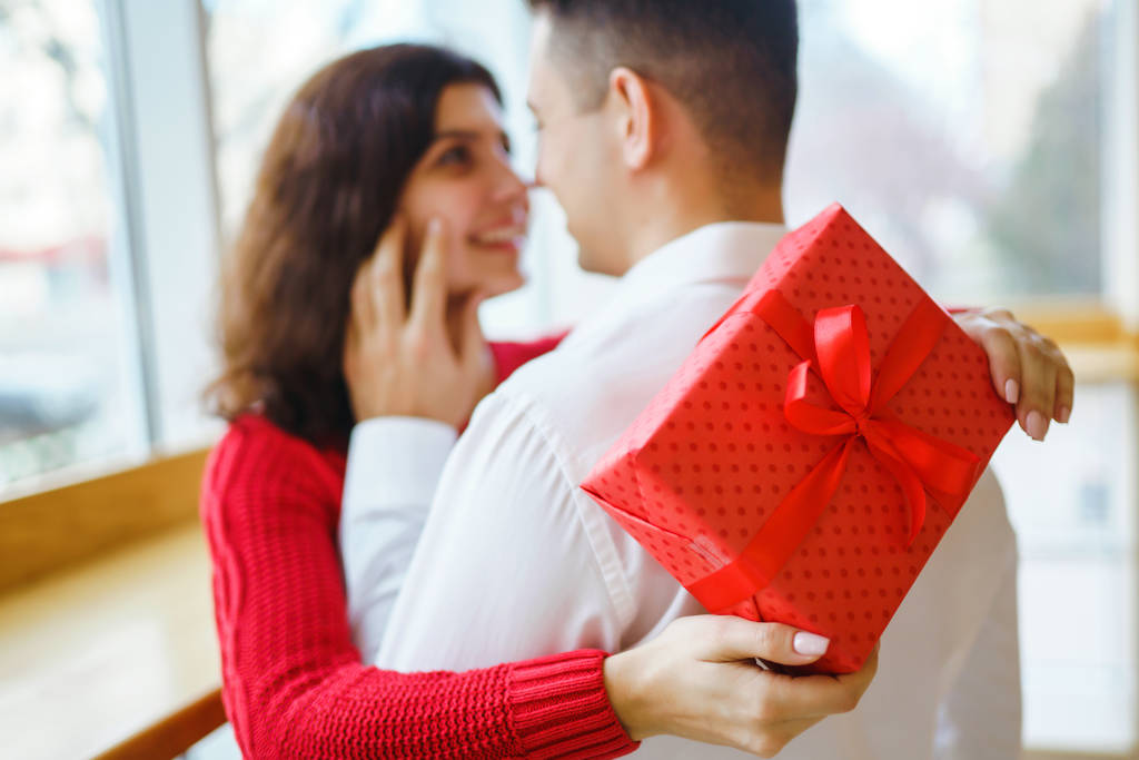 Close up of happy couple with christmas gift hugging. Cheerful couple with gift in hands enjoying together on Christmas eve. Lovers give each other gifts. Valentine's Day concept. - 写真・画像