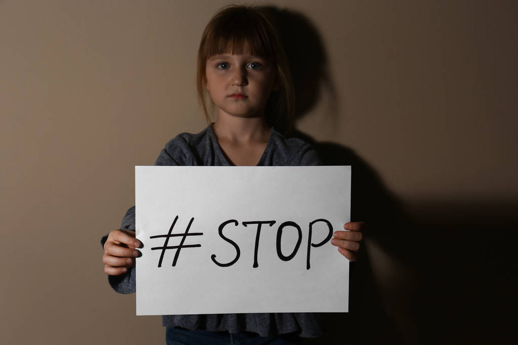 Κακοποιημένο κοριτσάκι με ετικέτα Stop κοντά σε μπεζ τοίχο. Εσωτερικό v - Φωτογραφία, εικόνα
