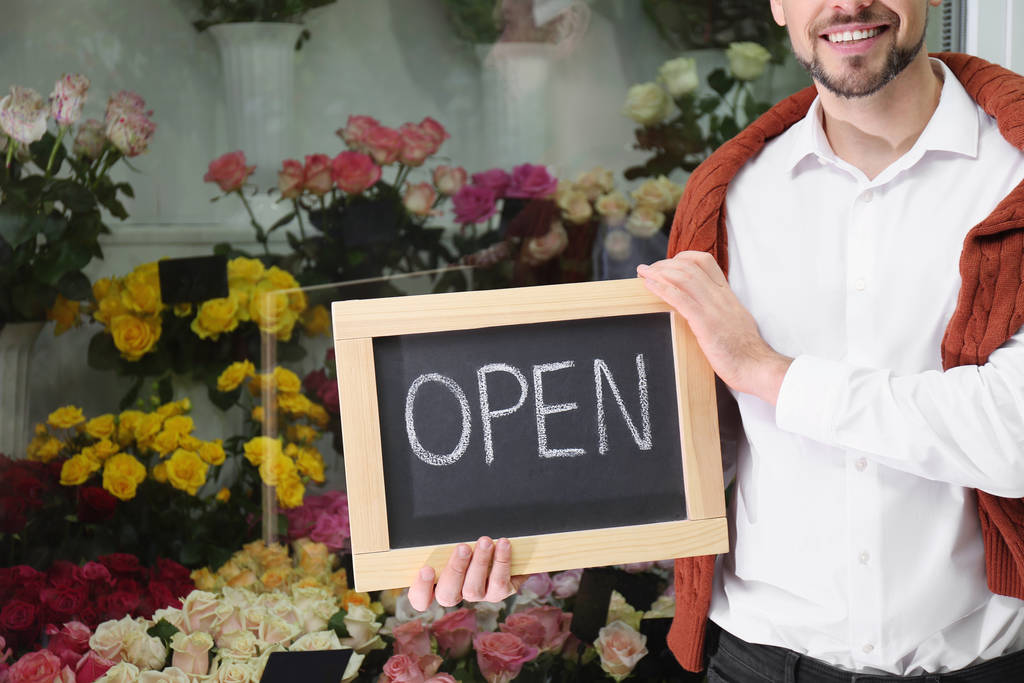 Власник магазину чоловічої статі тримає знак "Відкритий" у своїй крамниці квітів. - Фото, зображення