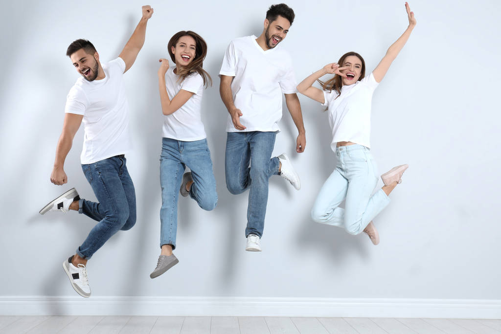 Gruppo di giovani in jeans alla moda che saltano vicino alla parete luminosa
 - Foto, immagini