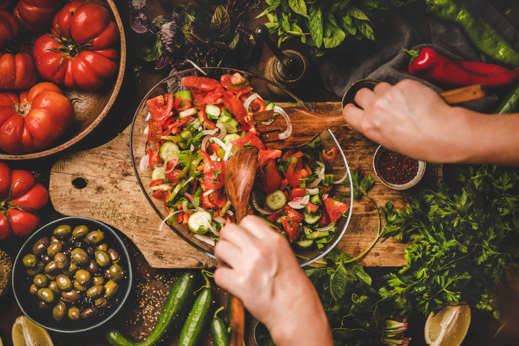 Плоскі руки жінок змішують турецький Chopard Salad, зроблений з свіжих овочів, трави з оливками і спеціями на тарілці, зверху. Середній Схід, середземноморська кухня, веганська здорова страва - Фото, зображення