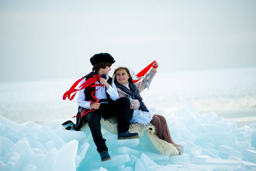 αγόρι και κορίτσι με θεματικές στολές με κόκκινες κορδέλες στο χειμερινό τοπίο - Φωτογραφία, εικόνα