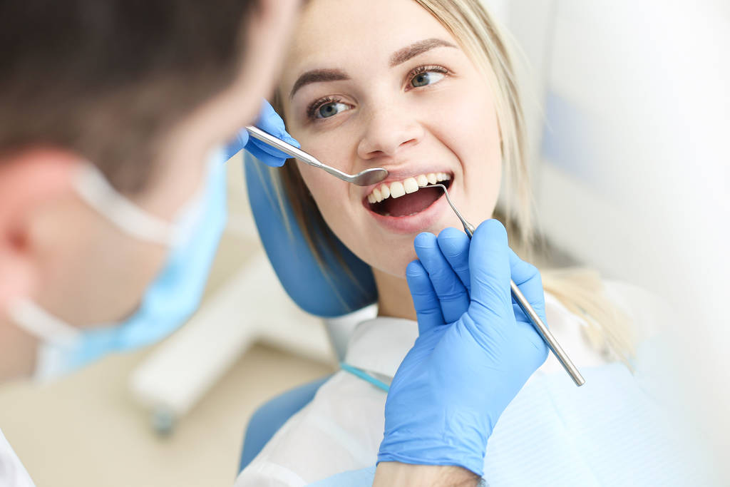 Słodka kobieta siedzi na krześle dentystycznym, podczas gdy dentysta bada jej zęby. Skupienie selektywne - Zdjęcie, obraz