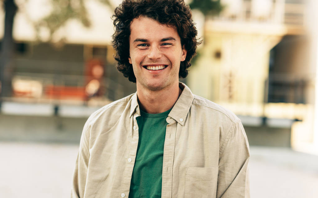 Venkovní horizontální portrét šťastného pohledného mladého muže, který se usmívá a pózuje pro reklamu, dívá se do kamery, stojí na městské ulici. Šťastný chytrý student pózující venku. Lidé, emoce - Fotografie, Obrázek