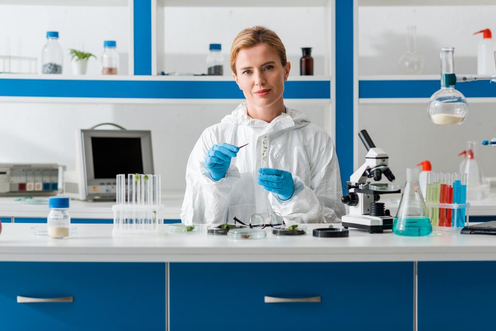 улыбающийся биолог держит пробирку и смотрит на камеру в лаборатории
   - Фото, изображение