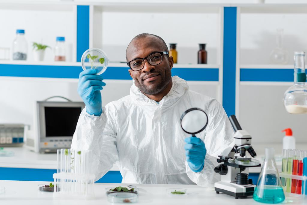 biólogo afroamericano sonriente sosteniendo lupa y hojas
  - Foto, imagen
