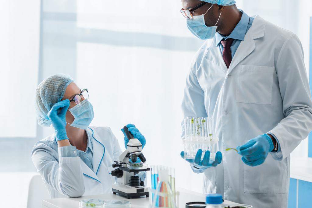 biólogos multiculturais em casacos brancos e máscaras médicas falando em laboratório
  - Foto, Imagem