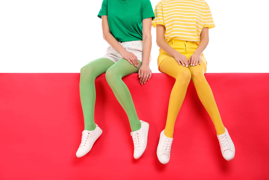 Frauen in hellen Strumpfhosen sitzen zusammen auf farbigem Hintergrund - Foto, Bild