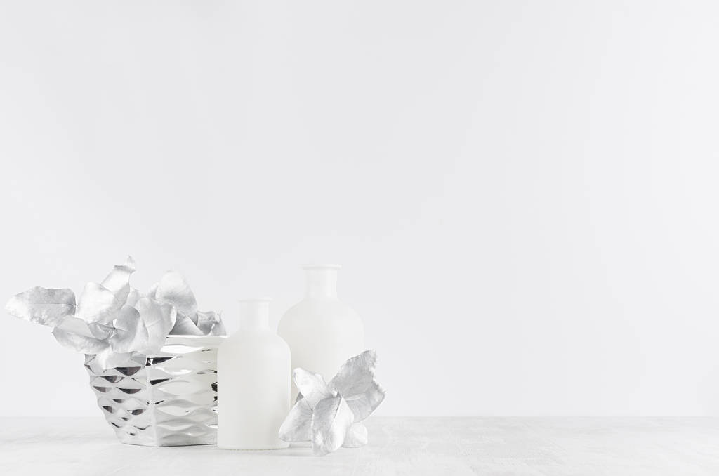 Decoraciones blancas contemporáneas simples para el interior: botellas de vidrio blanco, tazón de plata, hojas sobre fondo de madera blanca, espacio para copiar
. - Foto, Imagen