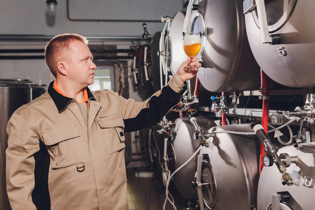 Зрілий чоловік вивчає якість крафтового пива в пивоварні. Інспектор, який працює на заводі з виробництва алкоголю, перевіряє пиво. Чоловік у винокурні перевіряє контроль якості пива
. - Фото, зображення