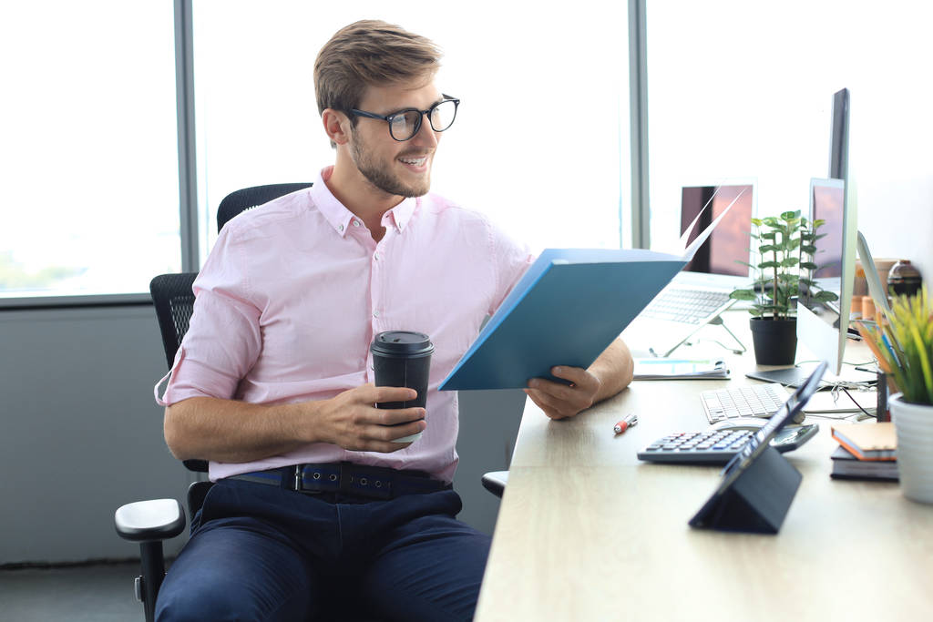 Jeune homme travaille avec des papiers alors qu'il est assis dans le bureau - Photo, image