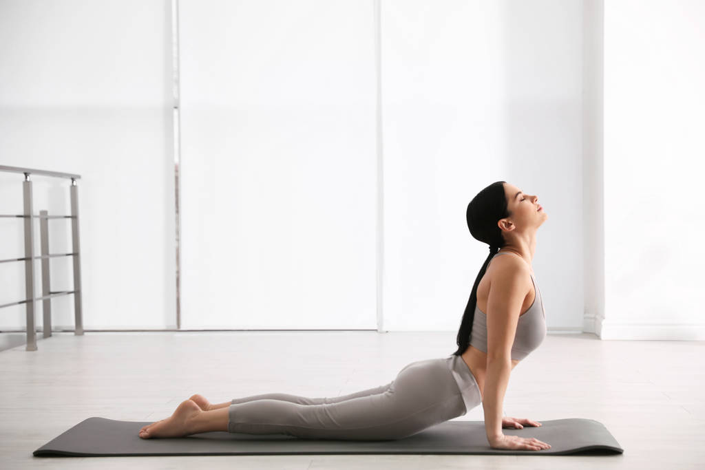 Jonge vrouw die cobra asana beoefent in yoga studio. Bhujangasana  - Foto, afbeelding