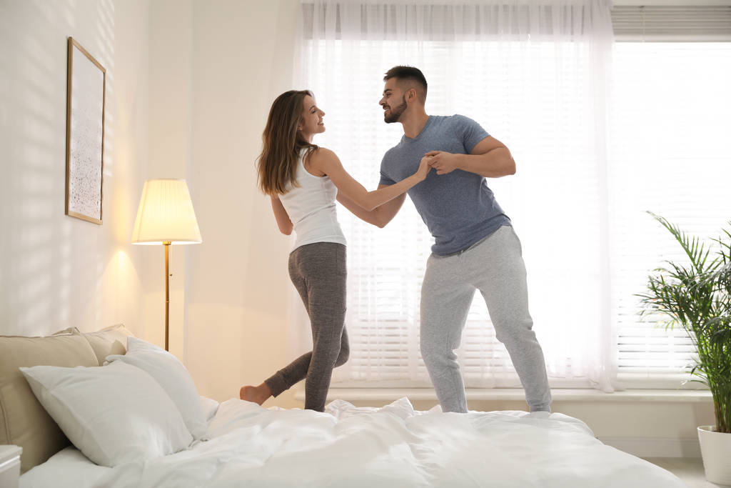 Adorável jovem casal dançando na cama em casa
 - Foto, Imagem