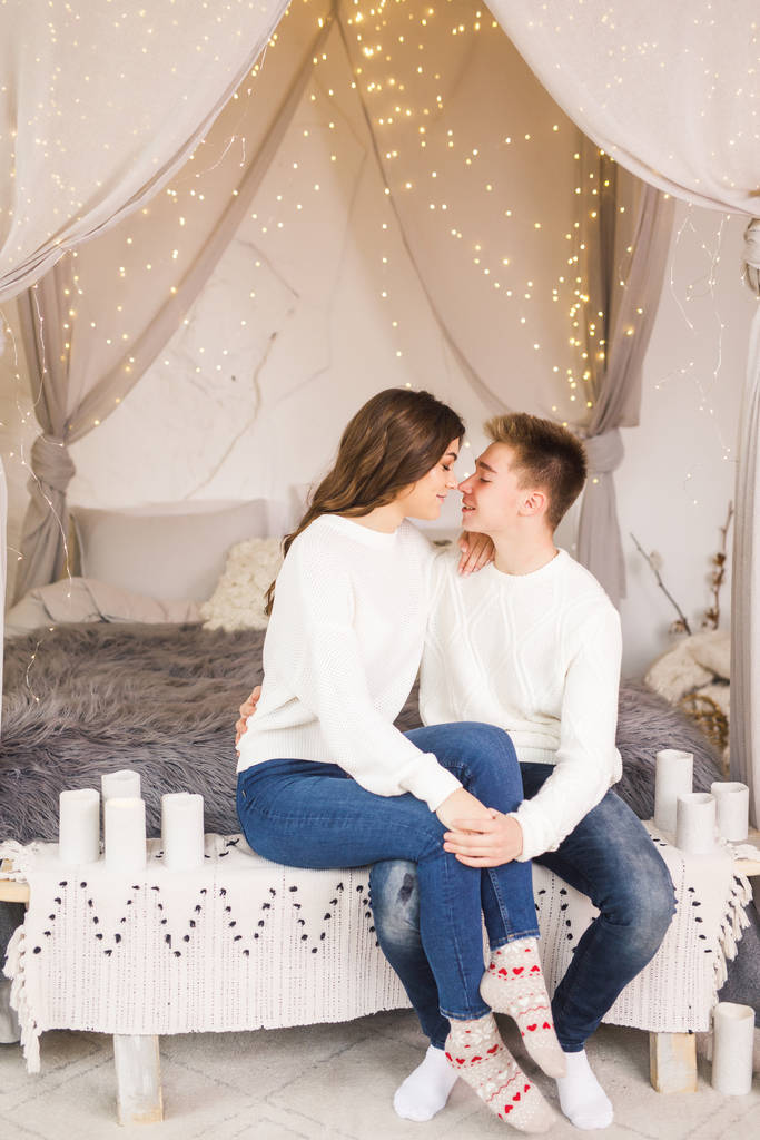 Młoda piękna para siedzi na łóżku w pięknym białym pokoju i uśmiecha się - Zdjęcie, obraz