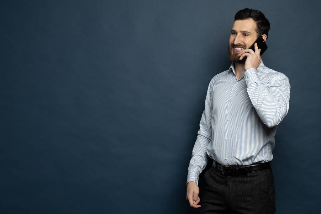 Un jeune homme souriant parle sur un téléphone mobile isolé sur fond bleu - Photo, image