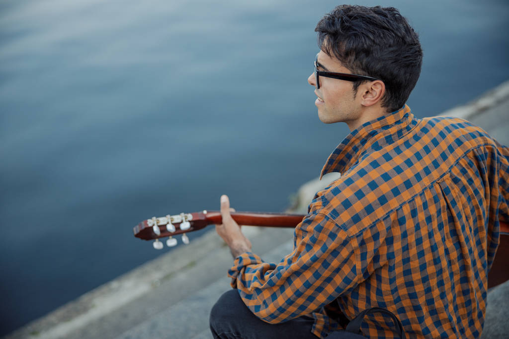 Gülümseyen adam nehir kenarında gitar çalıyor. - Fotoğraf, Görsel
