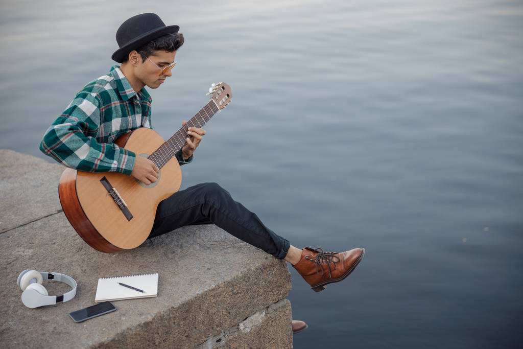 Мужчина-музыкант сидит с гитарой и ноутбуком на открытом воздухе
 - Фото, изображение